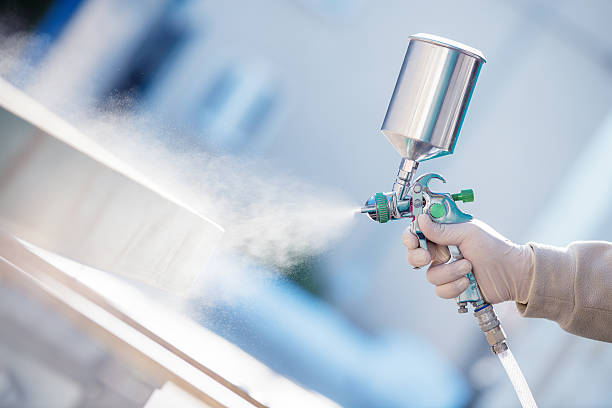 Hand holding a spray gun and painting wood in furniture factory